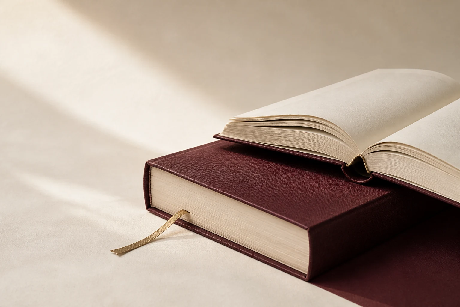 An open ivory book resting naturally on a burgundy clothbound volume